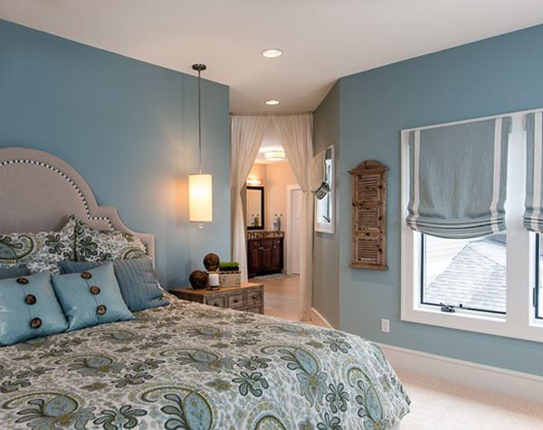light blue walls in bedroom, paisley bedspread and comforter, blue pillows, blue curtains, white ceiling, light carpet, light and inviting
